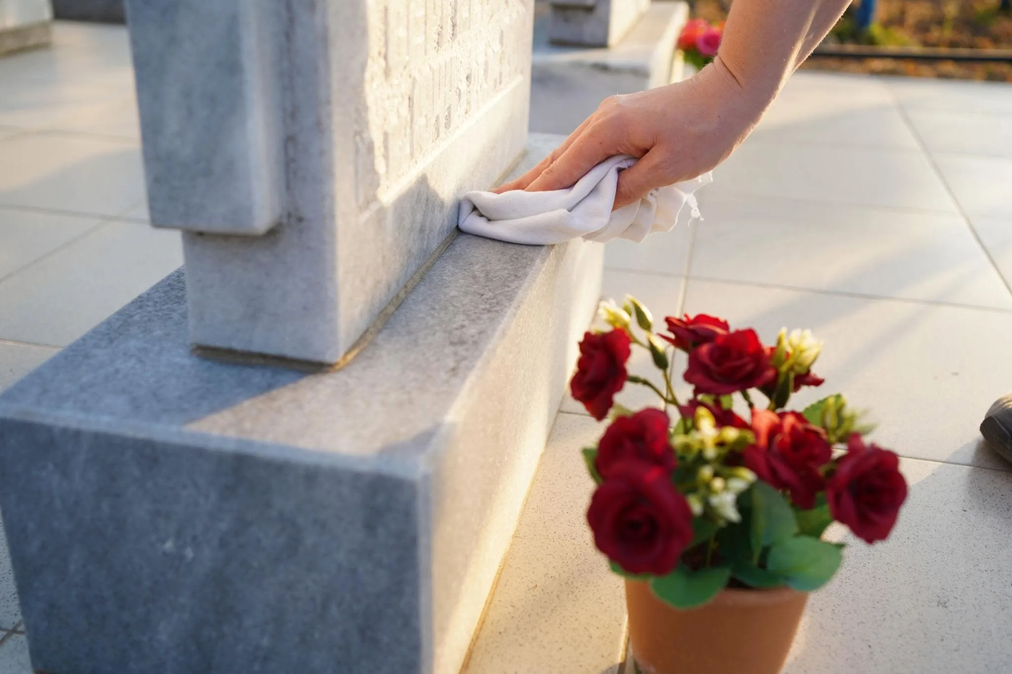 Wiping a headstone clean, with red roses beside it